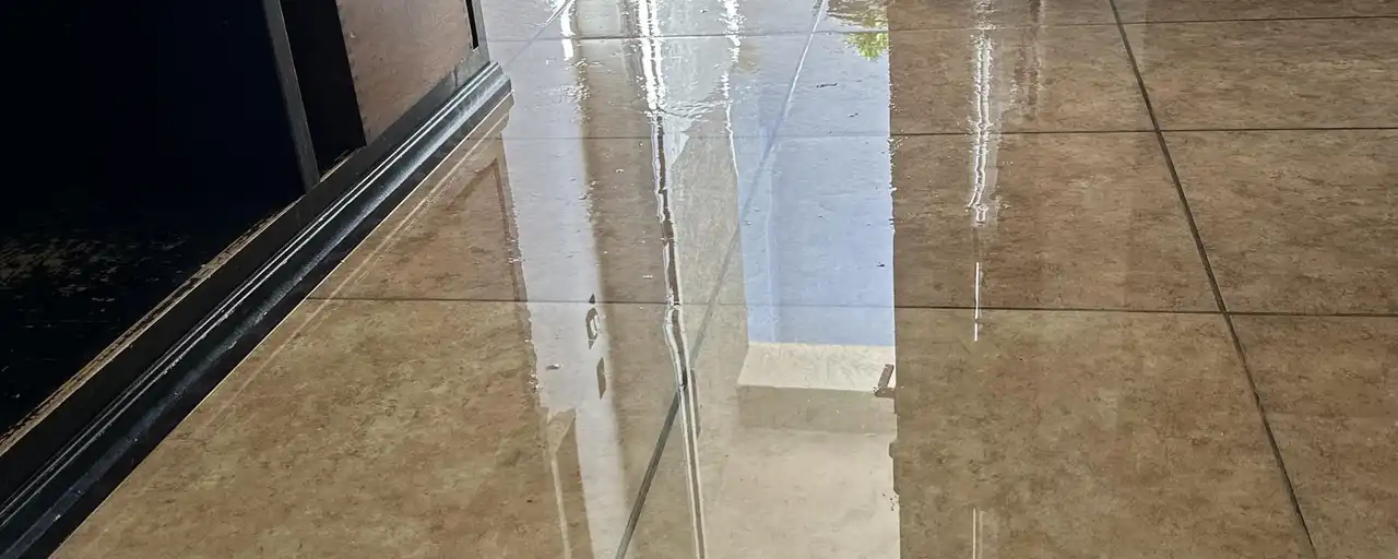 Standing water spread across a tile floor inside a home after a water leak