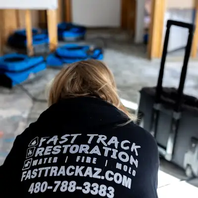 Fast Track technician in a company hoodie on a water damage job, with blue air movers drying the room